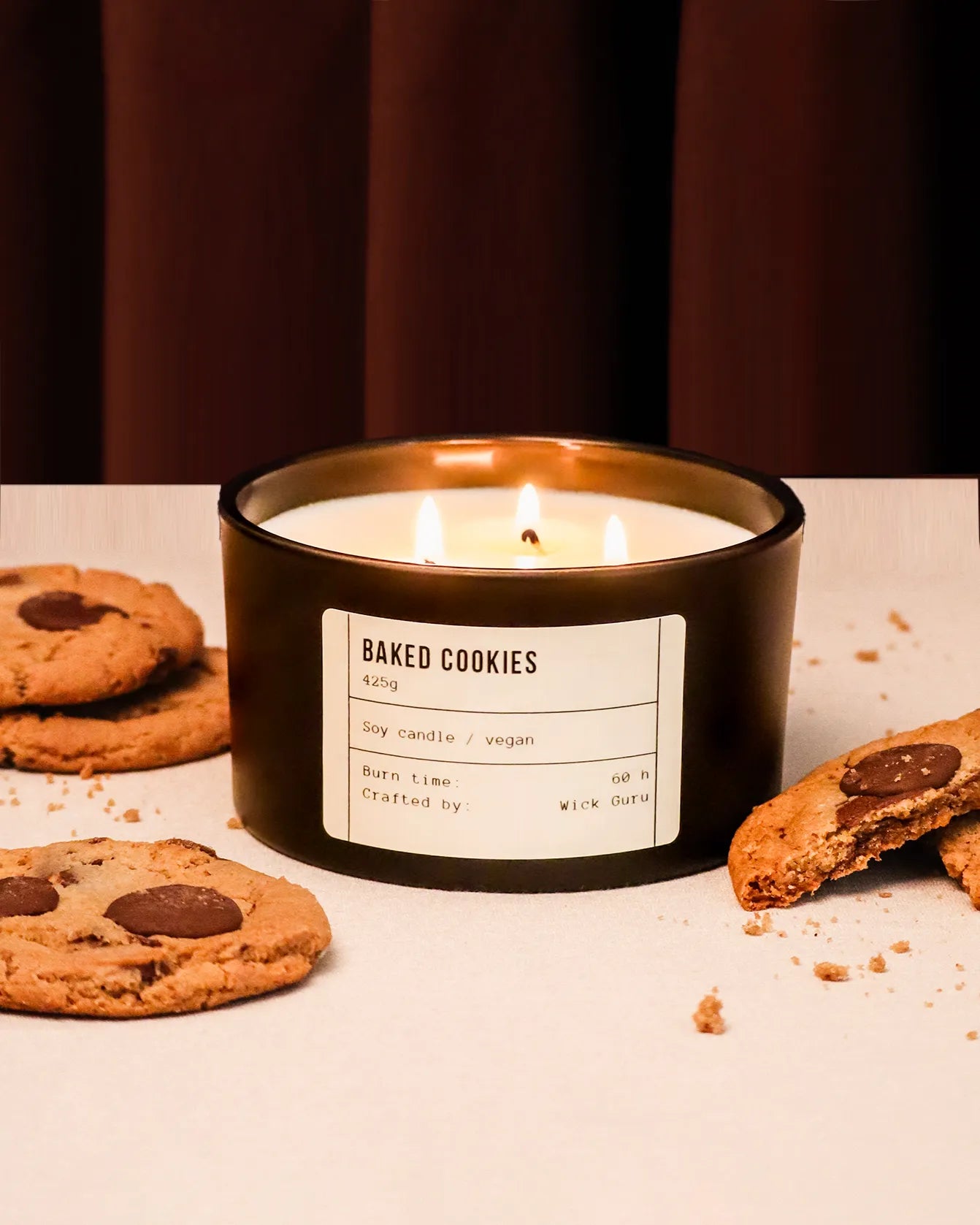 Candle labeled 'Baked Cookies' with cookies around on a white surface