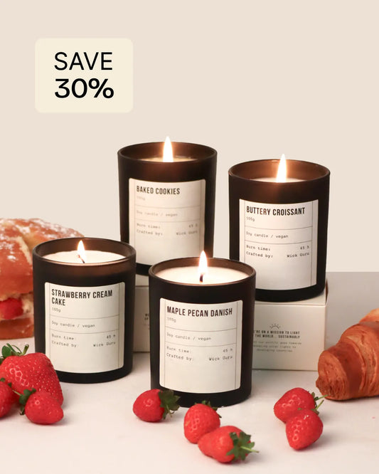 Four scented candles with labels and strawberries on a white surface