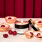 Candle labeled 'Cherry Barewell' with cherry tartlets on a red curtain background