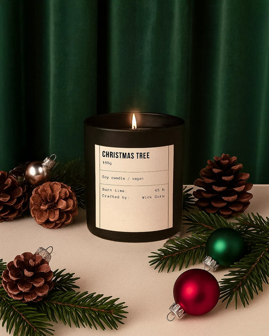 Black candle labeled 'Christmas Tree' with decorative pinecones and ornaments on a green curtain background