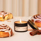 Candle labeled 'Cinnamon Rolls' with cinnamon rolls and a cinnamon stick on a light background