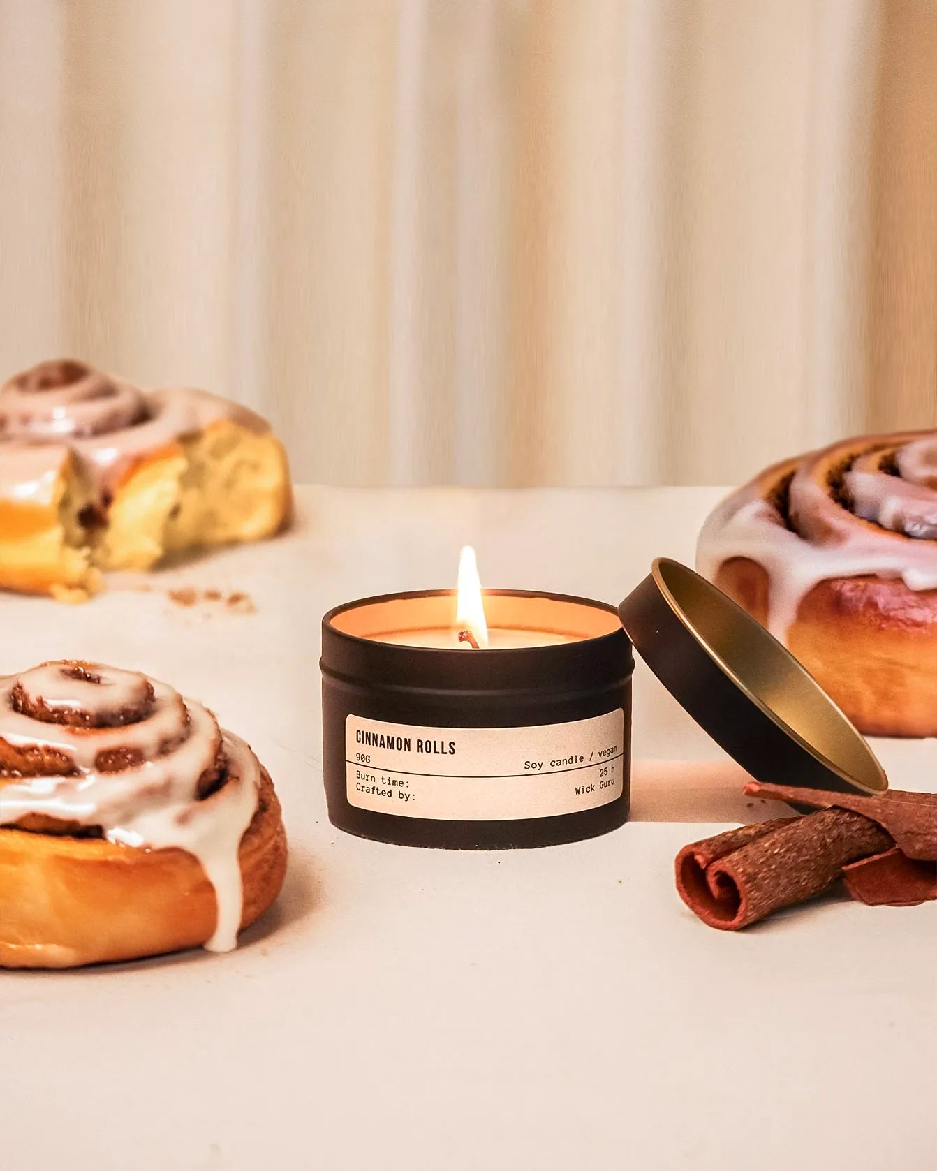 Candle labeled 'Cinnamon Rolls' with cinnamon rolls and a cinnamon stick on a light background