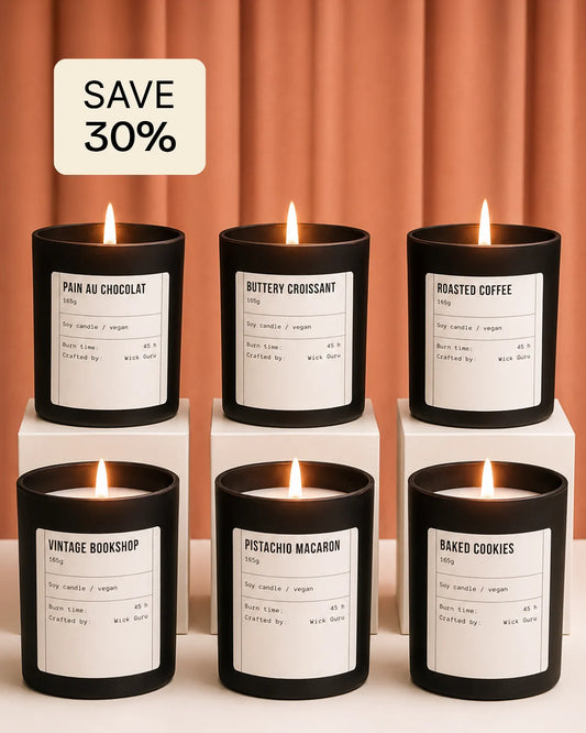 Set of six scented candles with labels on white cubes against a peach-colored curtain background.