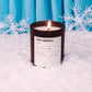 Candle labeled 'First Snowfall' in front of blue curtains with snowflake decorations