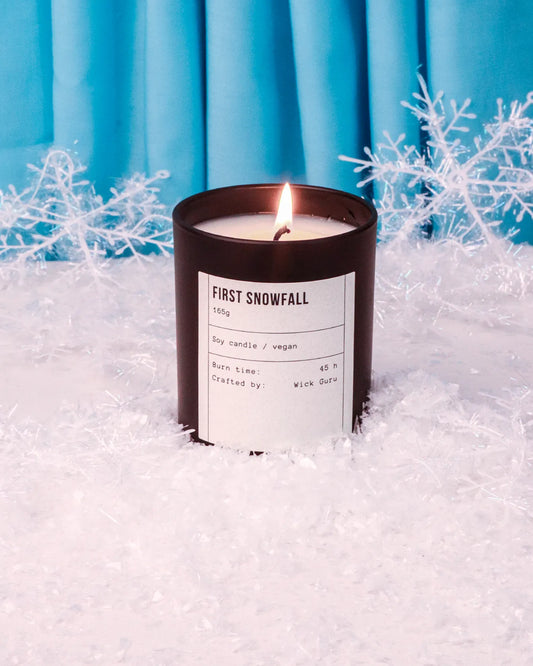 Candle labeled 'First Snowfall' in front of blue curtains with snowflake decorations