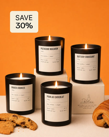 Four lit candles on boxes with labels, surrounded by cookies and pastries against an orange background.