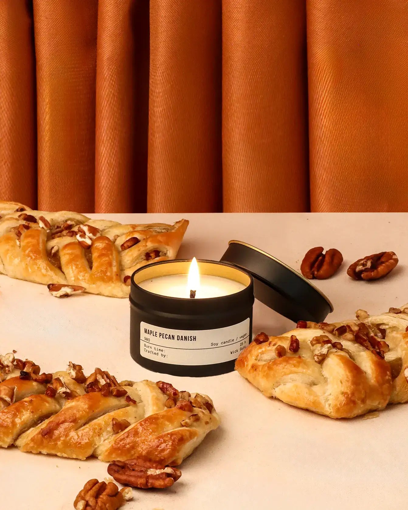 Candle labeled 'Maple Pecan Danish' with pastries and pecans on a neutral background
