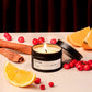 Candle with cinnamon, oranges, and berries on a dark background