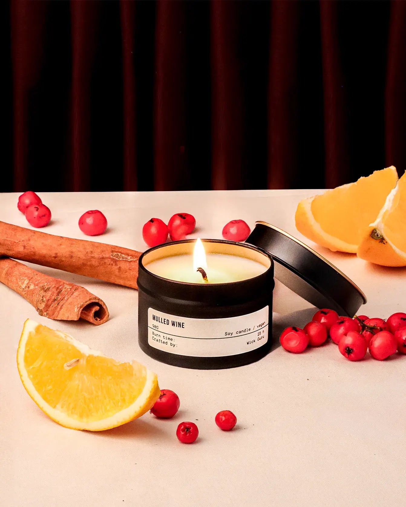 Candle with cinnamon, oranges, and berries on a dark background