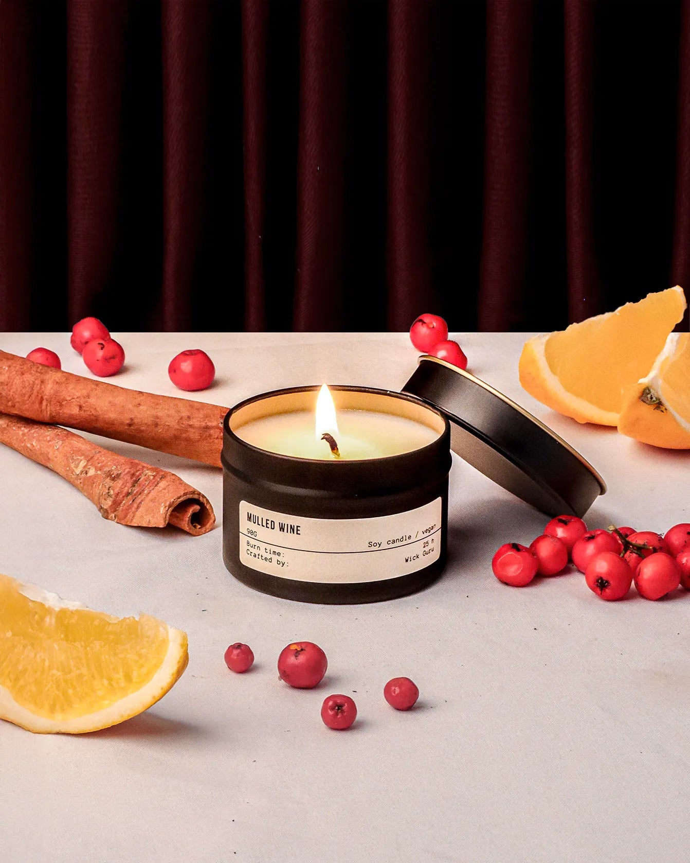 Candle with cinnamon sticks, oranges, and berries on a neutral background