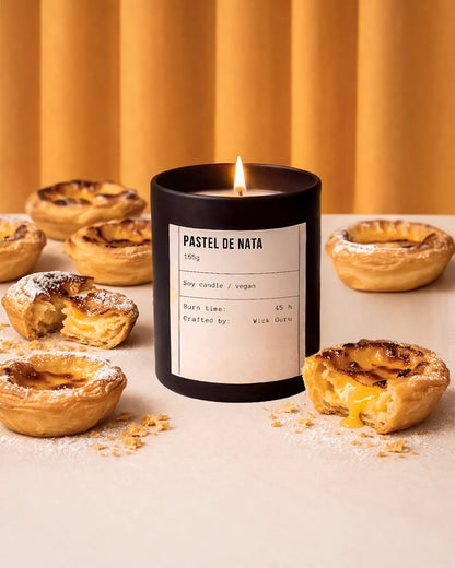 Candle labeled 'Pastel de Nata' surrounded by Portuguese pastries on a neutral background