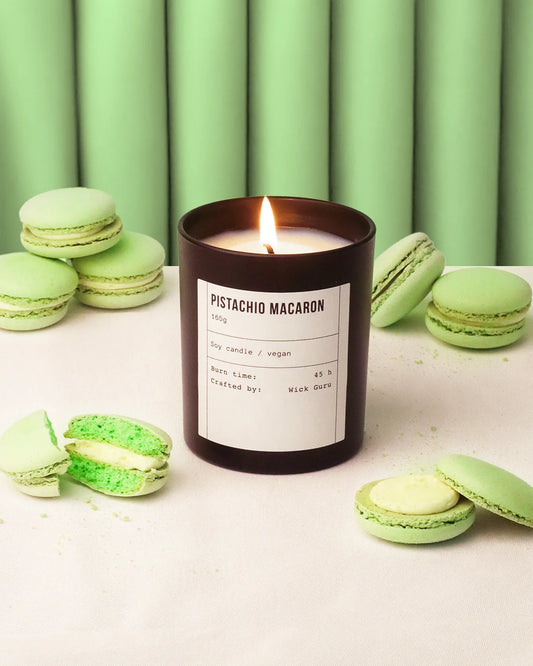 Candle labeled 'Pistachio Macaron' surrounded by green macarons against a green curtain background