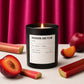 Candle labeled 'Rhubarb and Plum' with rhubarb and plum fruits on a pink curtain background