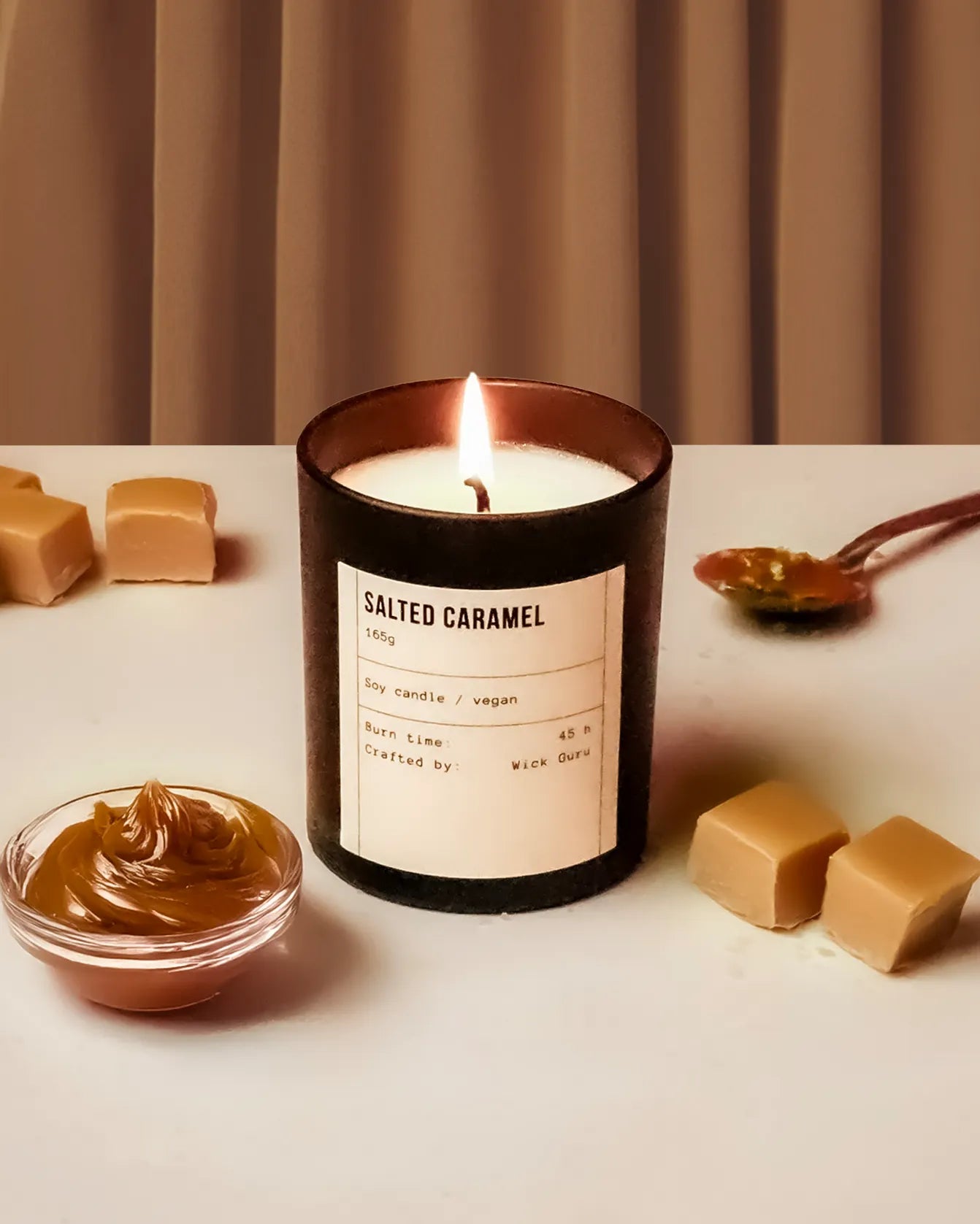 Salted caramel candle with caramel sauce and pieces on a white surface