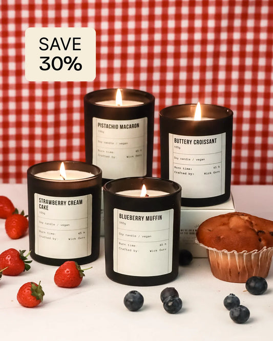 Four lit candles with labels on a white surface with berries and a muffin, against a red and white checkered background.
