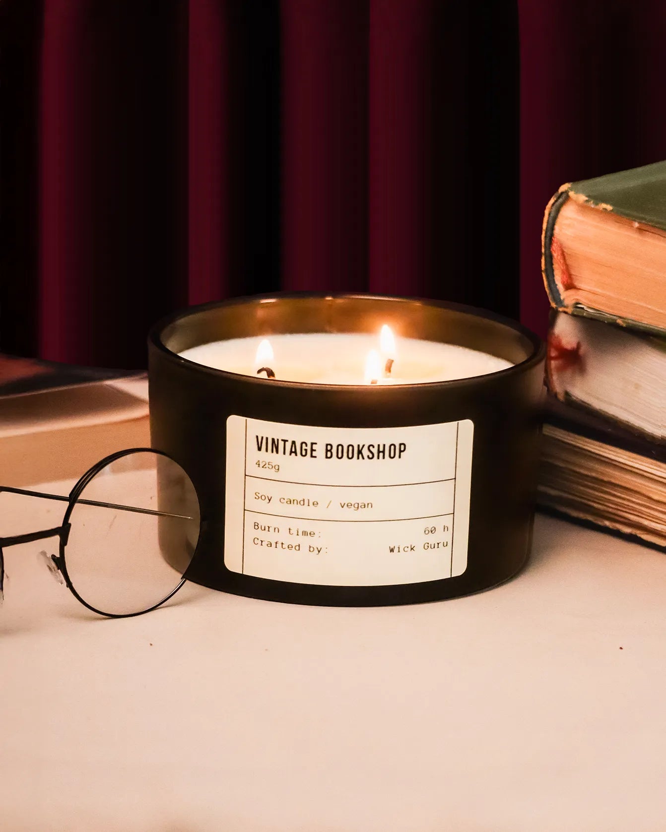 Candle labeled 'Vintage Bookshop' on a surface with books and glasses in the background