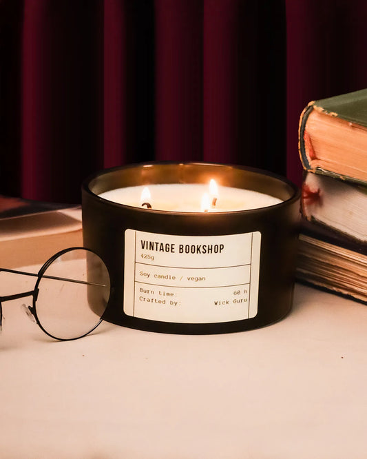 Candle labeled 'Vintage Bookshop' on a surface with books and glasses in the background