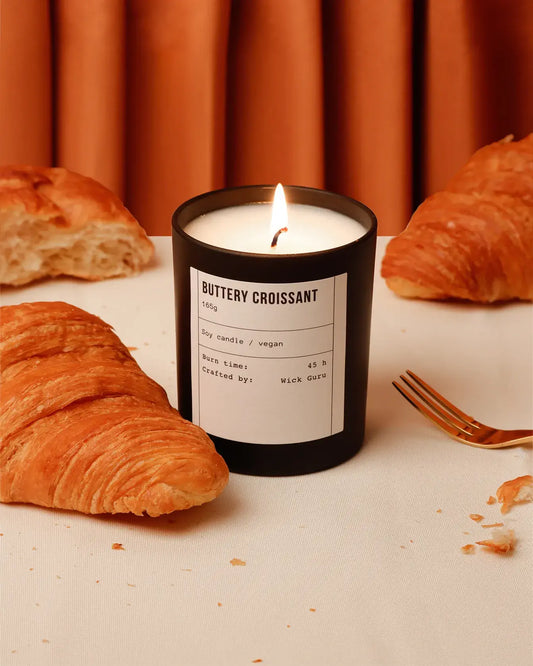 Candle labeled 'Buttery Croissant' with croissants and a fork on a table.