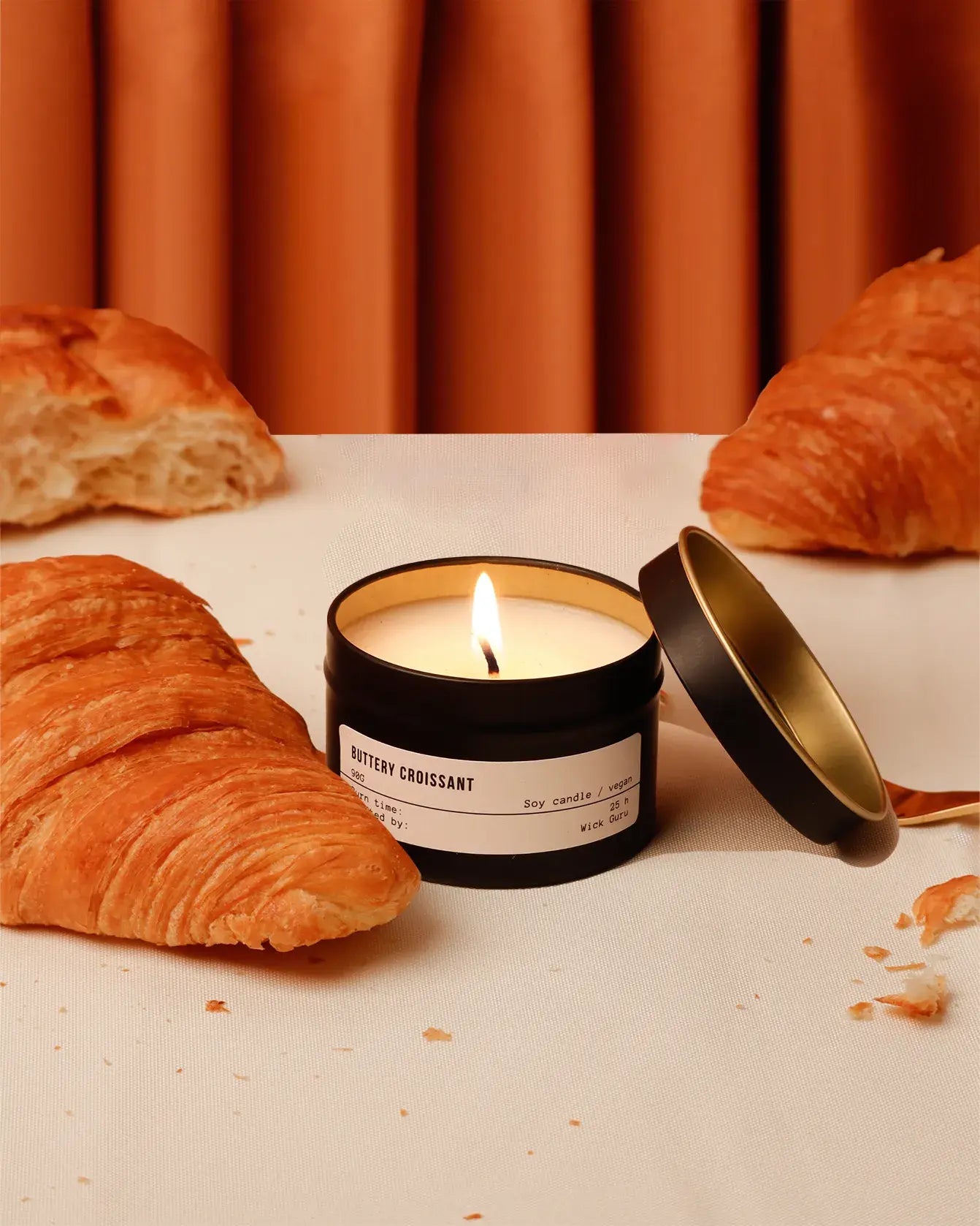 Candle labeled 'Buttery Croissant' with croissants on a table