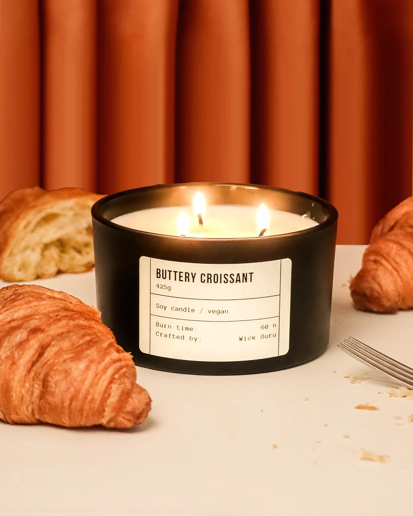 Candle labeled 'Buttery Croissant' with croissants on a table
