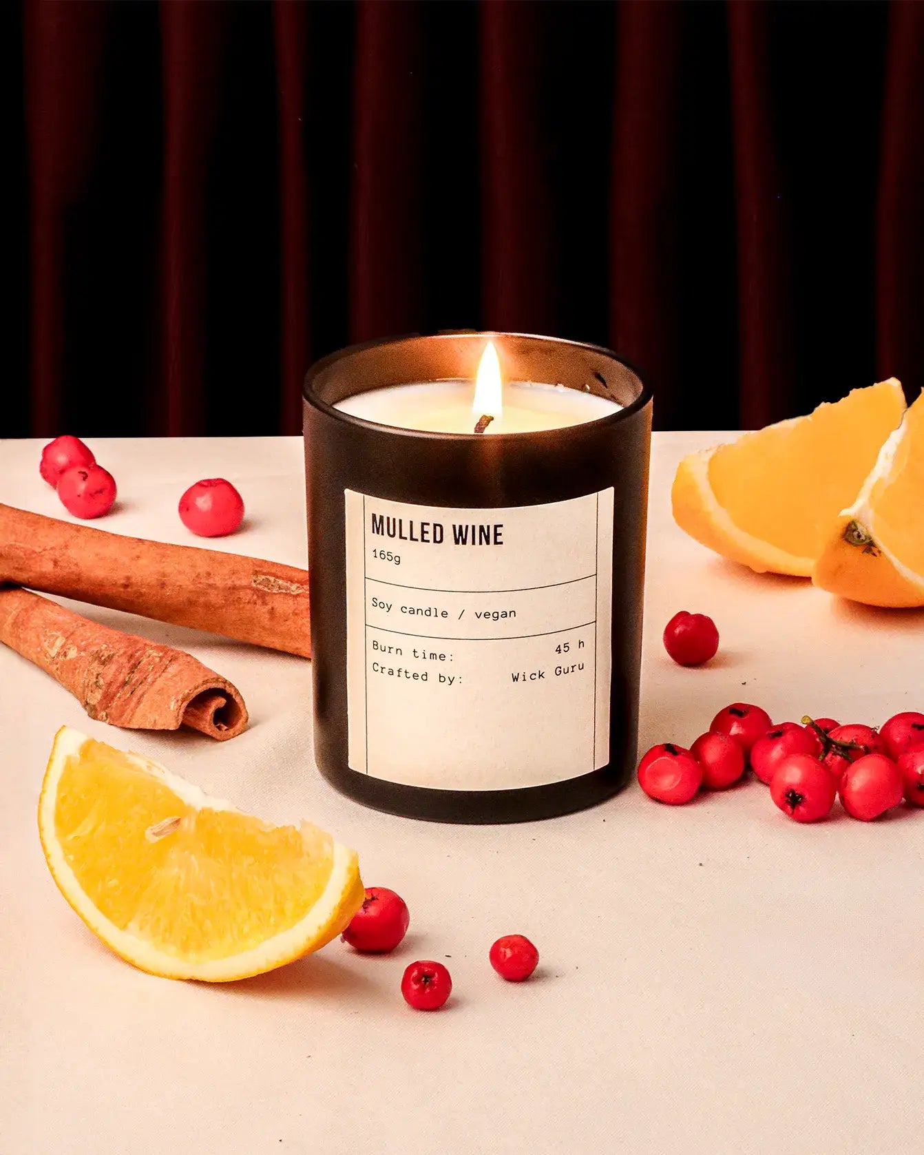 Candle labeled 'Mulled Wine' with cinnamon, oranges, and berries on a table.