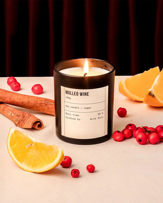 Candle labeled 'Mulled Wine' with cinnamon, oranges, and berries on a table.