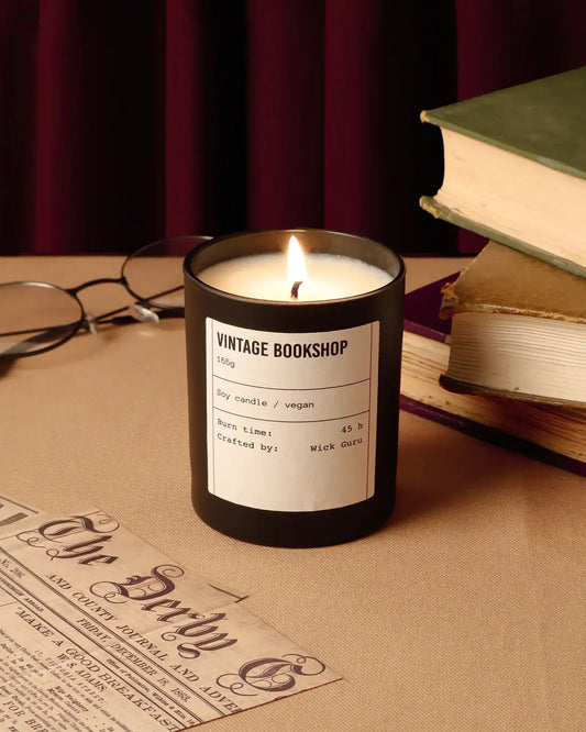 Candle labeled 'Vintage Bookshop' on a table with books and glasses.